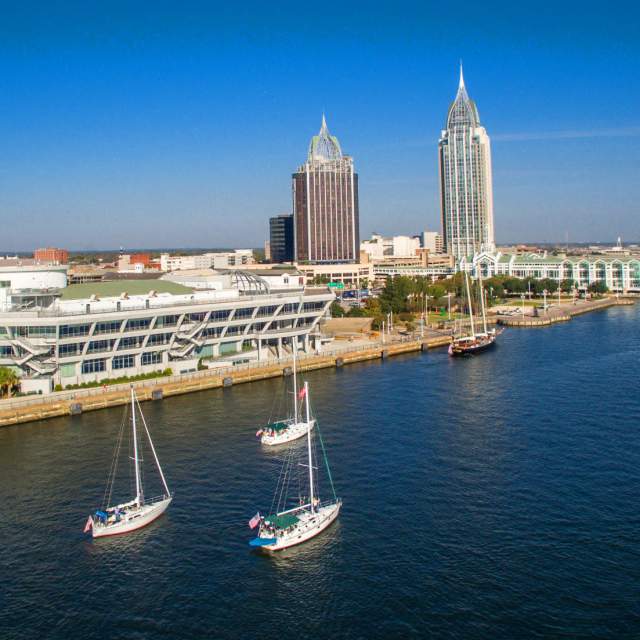 5 sailboats in the Mobile Bay with the city in the background