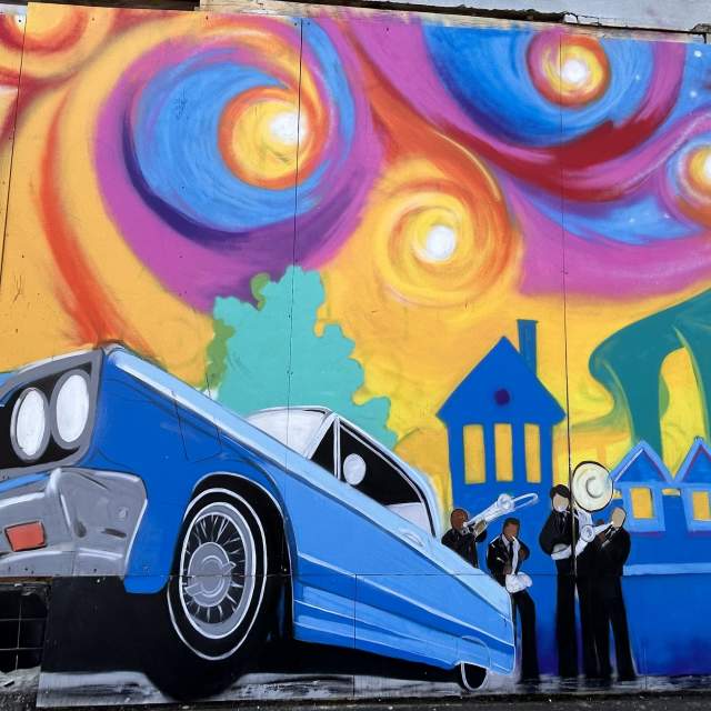 Mural of blue car in front of a rainbow sky and cityscape