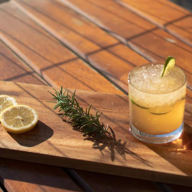 cocktail sitting on a wooden paddle with rosemary and lemon slices