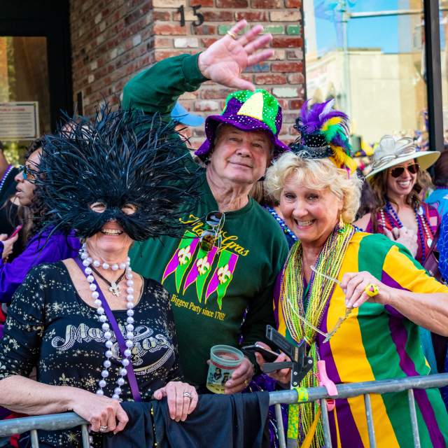 three elderly people dressed in Mardi Gras attire