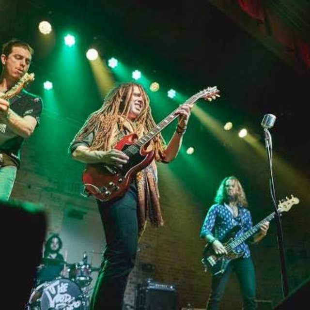 three men on stage playing guitar and singing