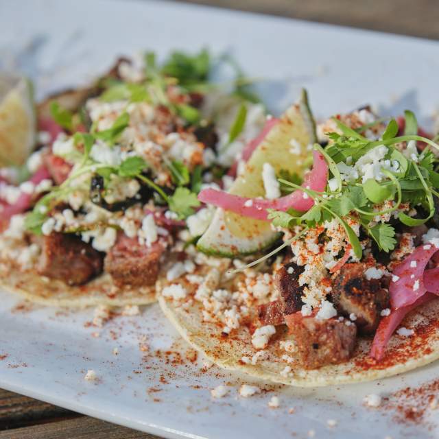 Plate of open-faced tacos with garnish on table