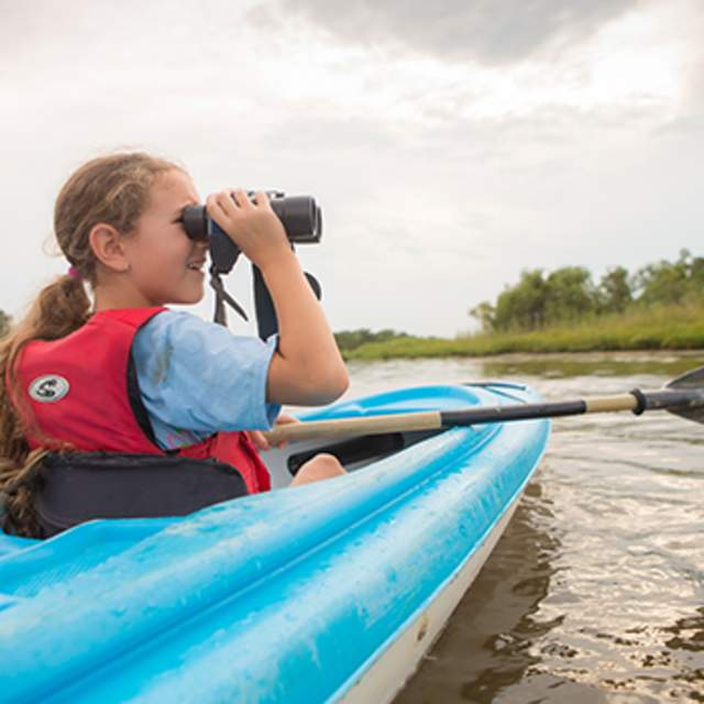 young girl in a kayak looking through binoculars
