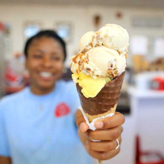girl holding up a triple scoop ice cream in a waffle cone