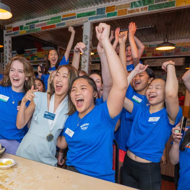 group of young females celebrating at a restaurant with hands in the air