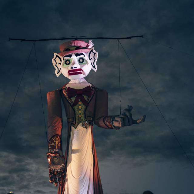 A large, illuminated puppet with a fierce expression is displayed against a cloudy evening sky.