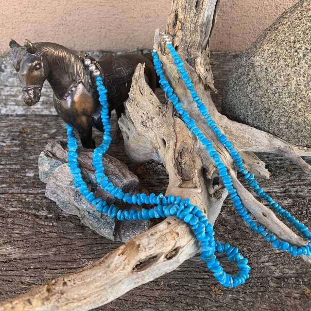 two beaded turquoise necklaces rest on a wooden stump