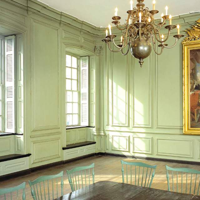 A formal meeting room with light green walls, a dark wood table, and a chandelier.