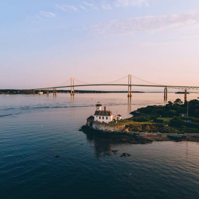 Aerial view of a lighthouse on a small island with a suspension bridge in the background