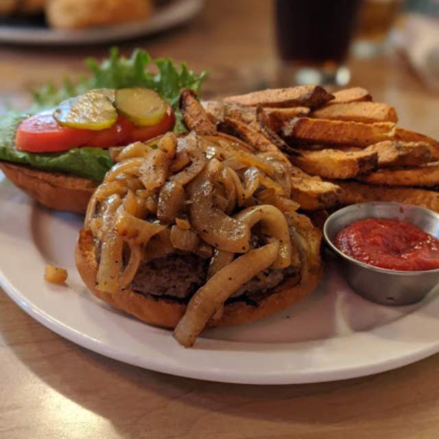 photo of a bison burger with caramelized onions and french fries served open faced on a plate