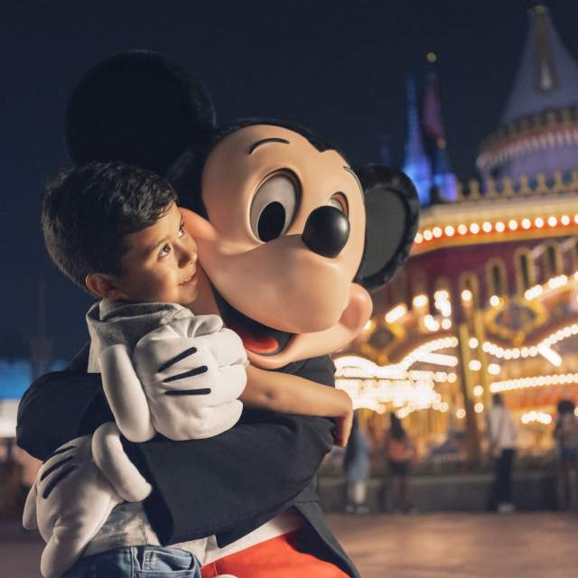 A boy hugging Mickey Mouse near the Prince Charming Regal Carousel at the Magic Kingdom in the Walt Disney World Resort.