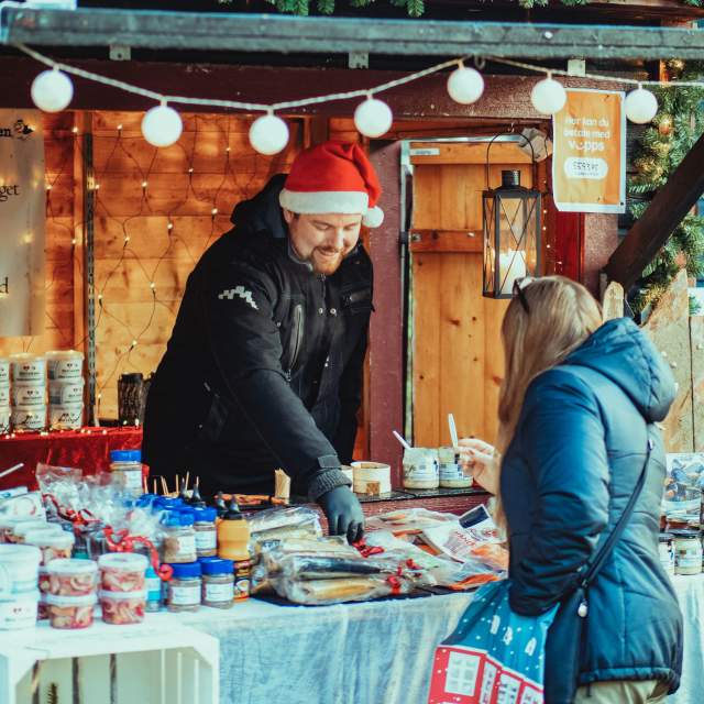 Mann som selger diverse delikatesser fra bod under julemarkedet i Sarpsborg. Foto.