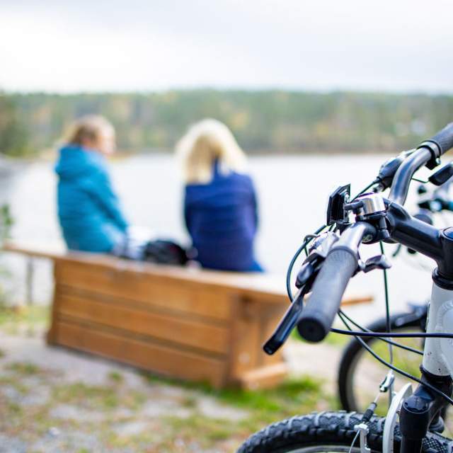 To jenter sitter på en krakk og ser ut mot havet. Syklene deres står i forgrunnen, og er i fokus.