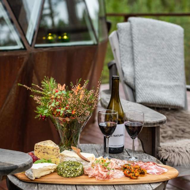 Ett brett med ost, vin og spekemat på terrassen til tretoppdoemn