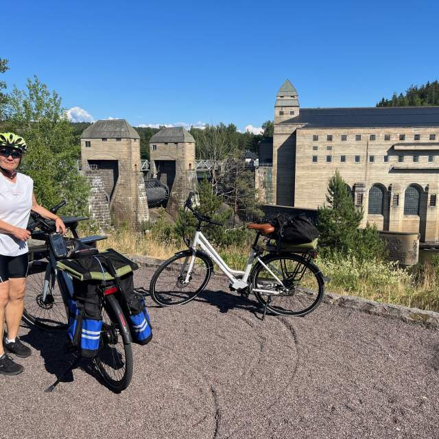 To oppakkede sykler og en dame foran mektige Solbergfoss kraftverk