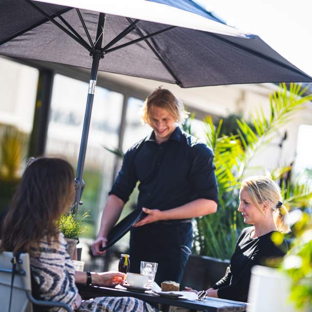 Kelner serverer to damer på uterestaurant