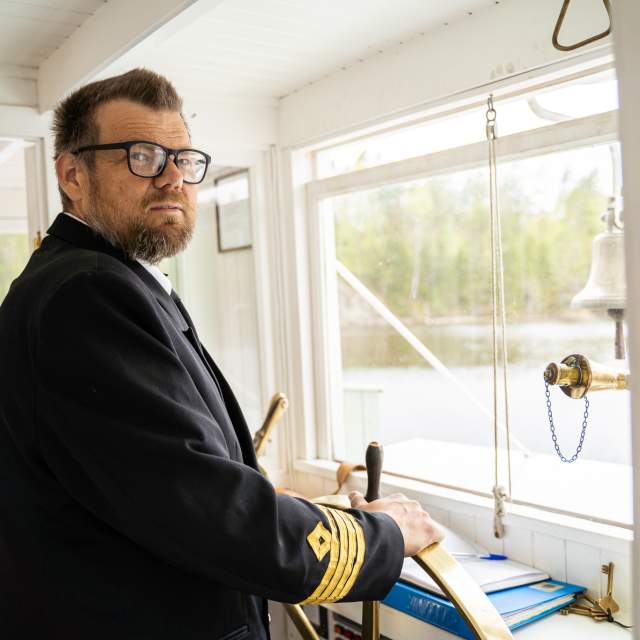 Kaptein i uniform styrer DS Turisten i Haldenkanalen