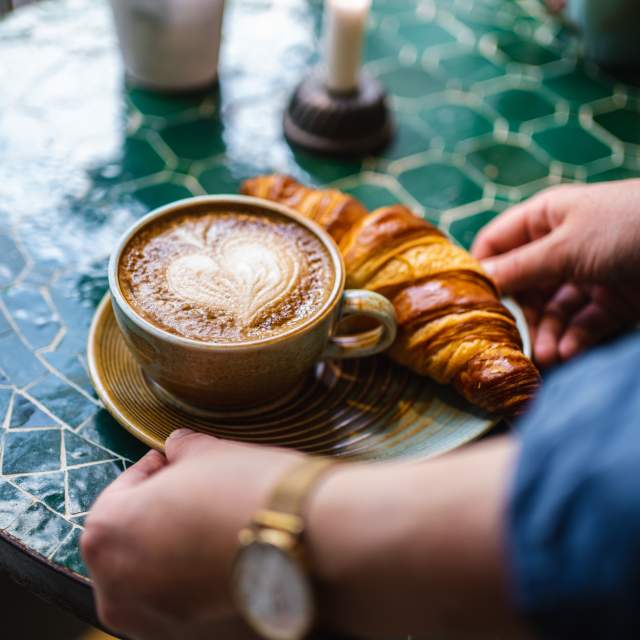 Kaffekopp med hjerteskum og en croissant servert på ett bord