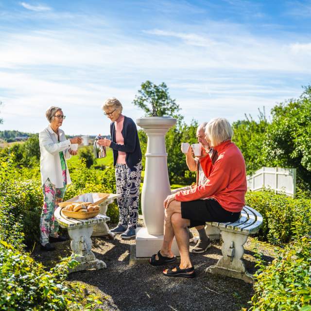 Damer som sitter i parken på Spydeberg prestegård og nyter kaffen og noe godt å bite i