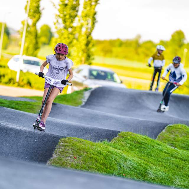 Tre barn på sparkesykkel i pumptrackbanen med bølgete asfalt