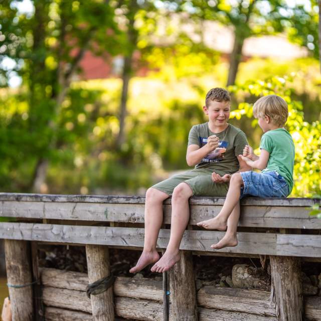 To gutter som sitter på en brygge og leker stein saks papir