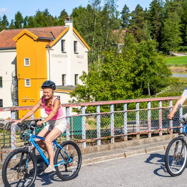 Ett par sykler over brua med Strømsfoss mølle i bakgrunn