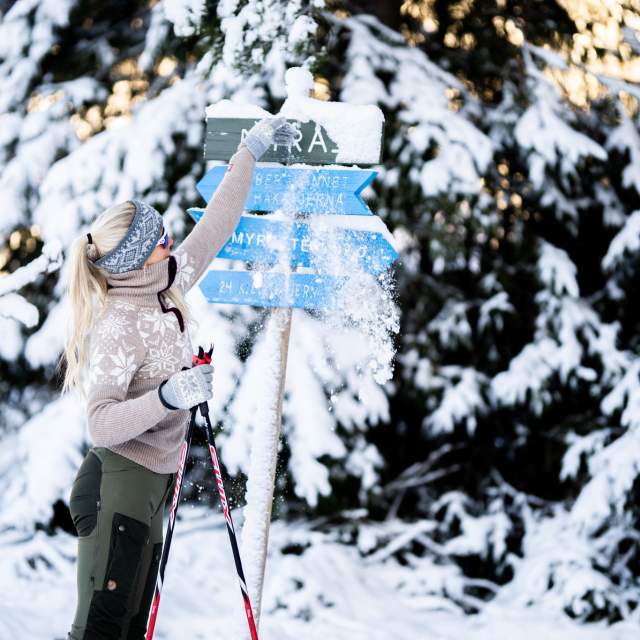 En dame børster av snøen på skiløypeskilt
