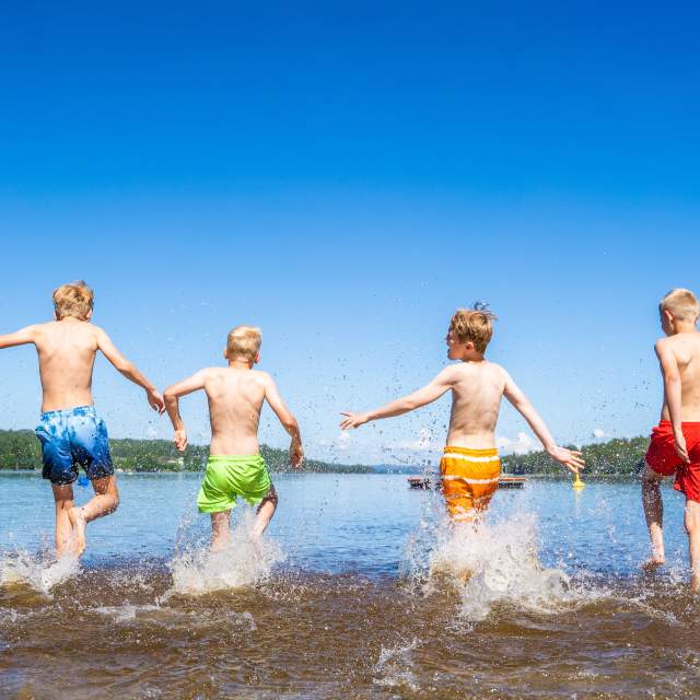 4 gutter i fargerike shorts som løper ut i vannet