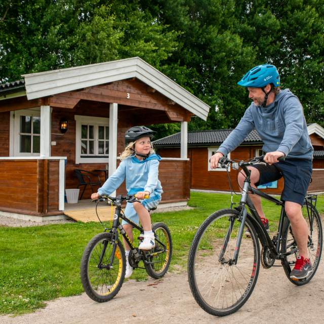 En mann og en jente på sykkel foran en camping hytte.