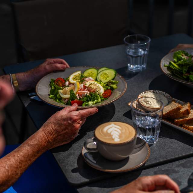 Bilde av en salat og en kopp kaffe, mens gjester sitter og spiser på en kafé.