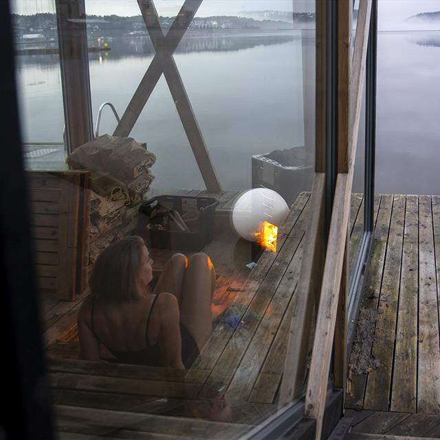 Kvinne sitter i en flytende badstu og ser utover vannet