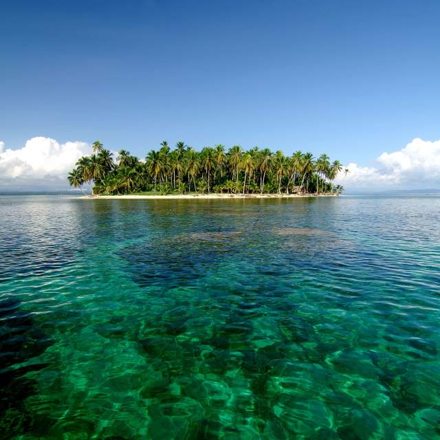 Small island covered in dense vegetation, with a few sandy beaches visible. The water is shallow and clear, with a visible sandy bottom.