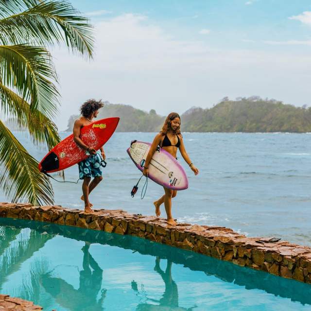 Couple walking near a pool with surfboards, Isla Grande beach can be seen in the background