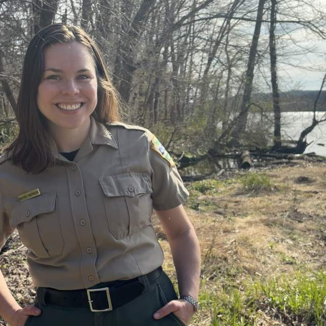Woman posing for a photo in front of trees at a lake