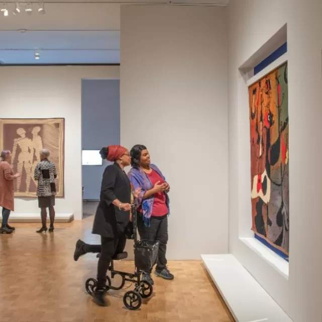 Two women, one with a scooter holding up her leg for accessibility purposes, looking at a piece of art in the Barnes Foundation in Philadelphia, Pennsylvania