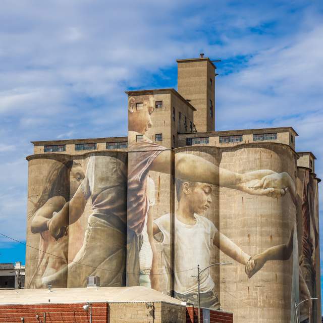 a mural painting of children holding hands painted on HD Lee Flour Mill in Salina Kansas. It is titled Mural at the Mill and painted by Guido Van Helten