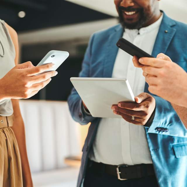 Three people look at their mobile phones and tablets while strategizing a digital services campaign.