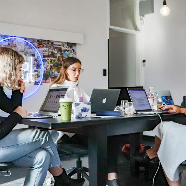 Three women work on their laptops while seated at the same table.