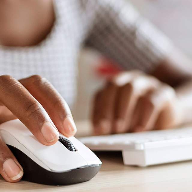 A woman controls a computer with a white and black mouse.