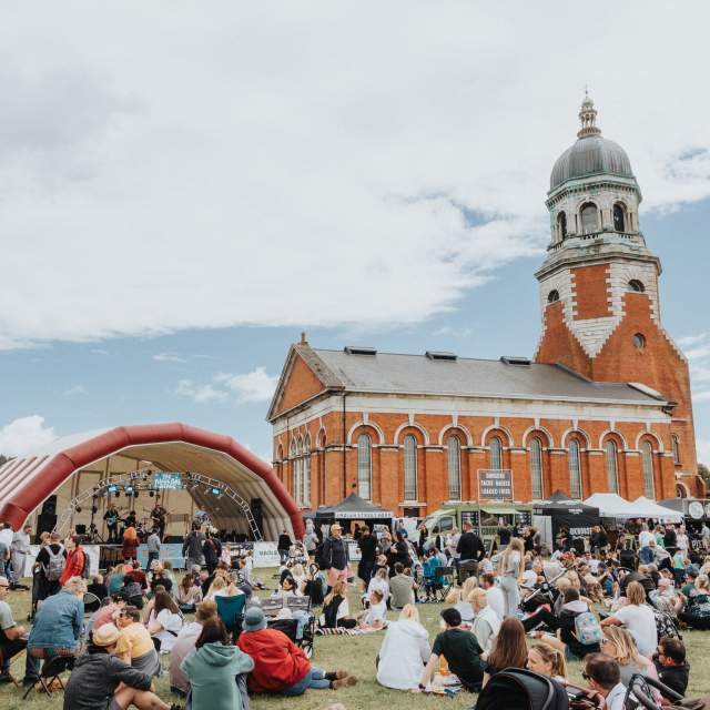 Groups of people sitting on grass in front of stage or walking around the grounds of Royal Victoria Country Park at The Big Eat Festival
