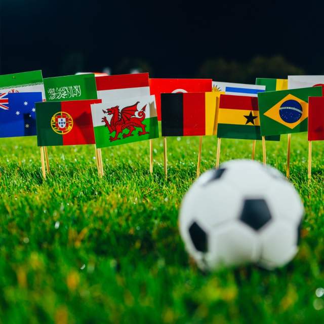 Football on grassy field in front of collection of flags of the world including England, Wales, Portugal, Germany and more