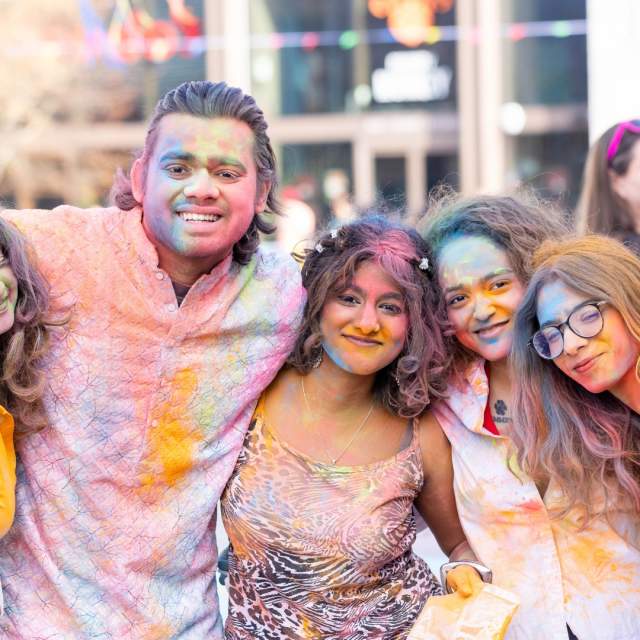 Group of friends covered in colourful powders posing for a photo at Holi event 2025