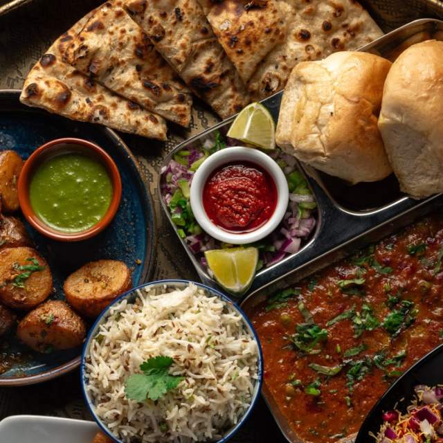 Mixture of vegetarian Indian dishes on large round serving plate including naan bread, lentil curries and chutneys