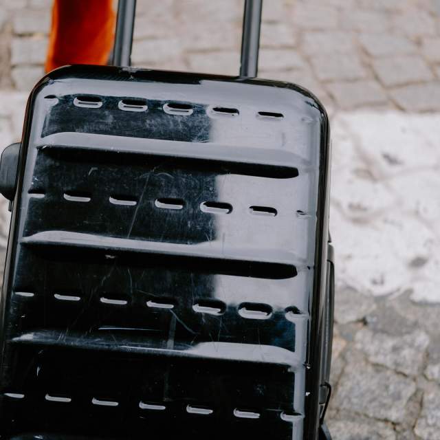 Close up of a black suitcase and someones feet pulling it along