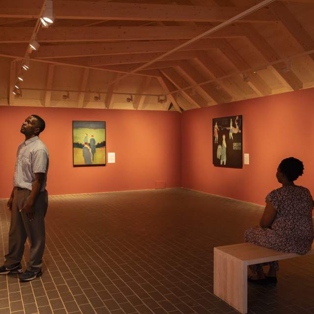 A couple stand in the gallery at Charleston, looking at artwork hanging on orange colour walls