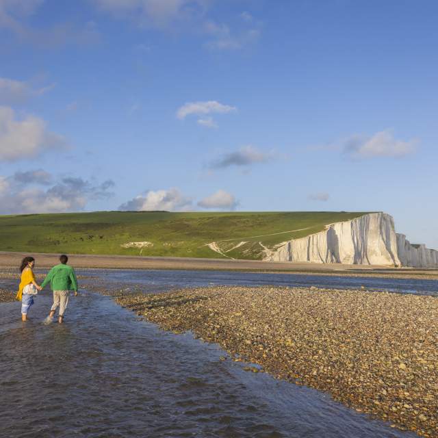 A couple walk in the water at low tide near Seven Sisters