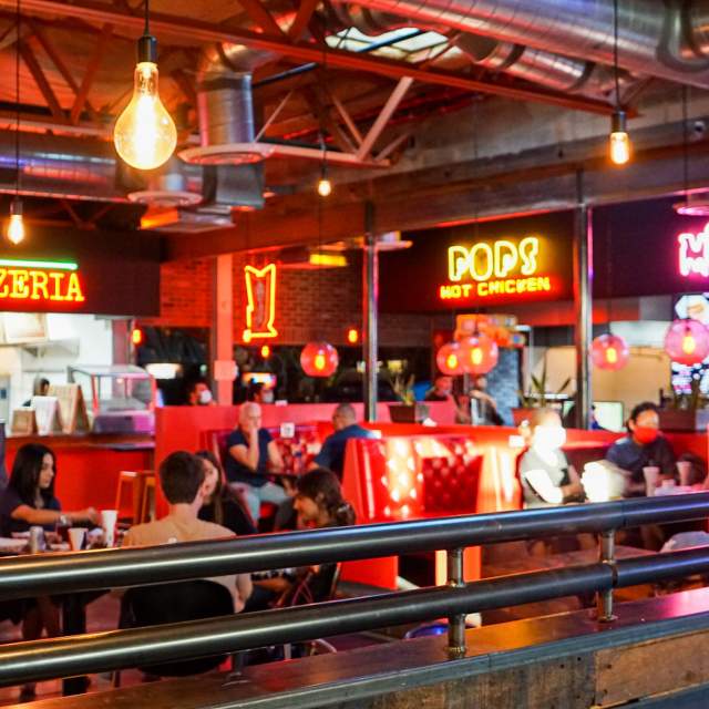 Interior of a retro, food court restaurant with people sitting at tables under bright neon restaurant signs