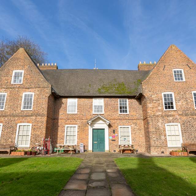 A thatched manor house with gardens and gates from the front