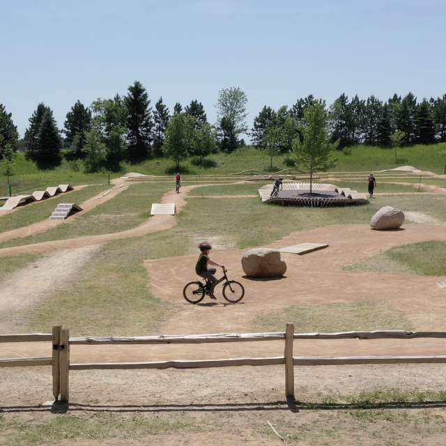 Carver Lake Bike Park outdoor trail showing bikers maneuvering different skill challenges.