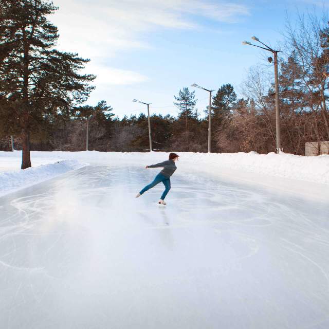 Figure skater performing on an outdoor ice rink surrounded by a snowy outdoor scene.
